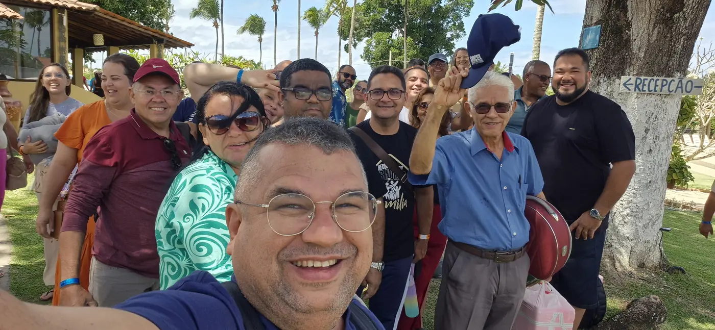 Edson tirando uma selfie com uma turma grande de clientes sorrindo no jardim do hotel